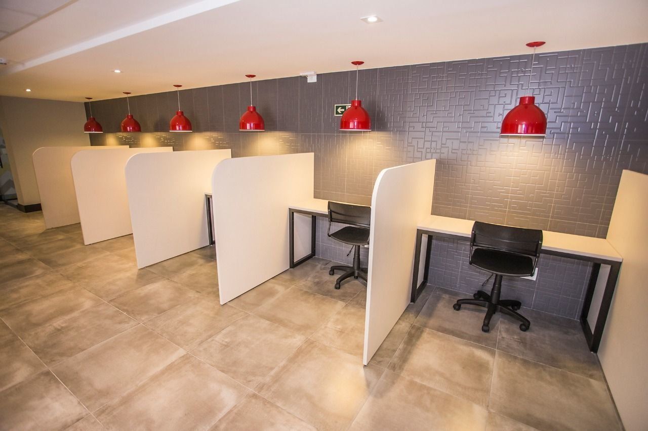 A modern office space with cubicles, red pendant lights, and a grey-tiled wall.
