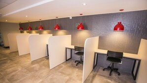 Un espace de bureau moderne avec des cloisons, des suspensions rouges et un mur recouvert de carreaux gris.