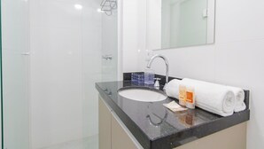 A modern bathroom with a glass shower enclosure, a black countertop sink, and a white towel. - Studio com Sacada All You Need ALL0305 (Curitiba)
