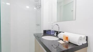 Un baño moderno con cabina de ducha de vidrio, un lavabo con encimera negra y una toalla blanca.