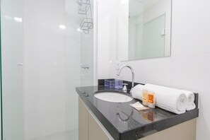 Uma casa de banho moderna com cabine de duche em vidro, lavatório com bancada preta e toalha branca.