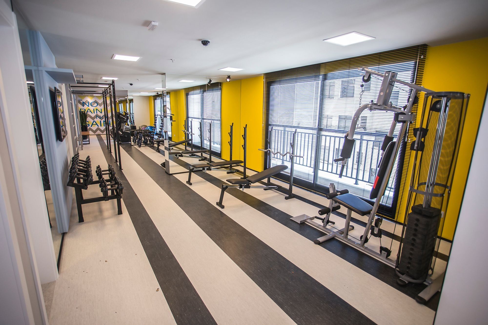 Un gimnasio con equipo de ejercicio, espejos y una pared amarilla.