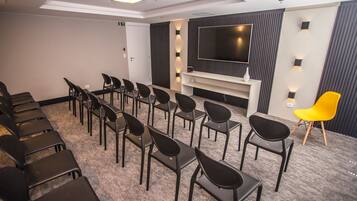 A conference room with rows of chairs, a large flat-screen TV, and a small white table with a vase.