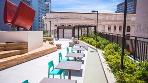 An outdoor seating area with tables and chairs, a red sculpture, and a building with classical architecture in the background. - Studio com Sacada All You Need ALL0305 (Curitiba)
