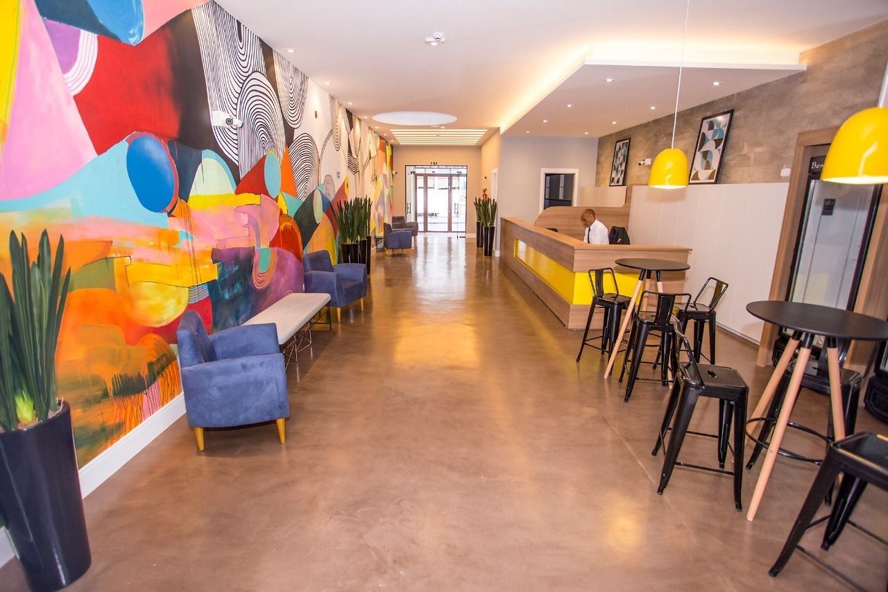 Un moderno vestíbulo de hotel con un mostrador de recepción alargado, sofás azules y un mural abstracto y colorido en la pared izquierda.