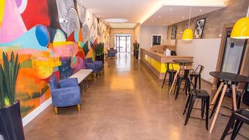 Un moderno vestíbulo de hotel con un mostrador de recepción alargado, sofás azules y un mural abstracto y colorido en la pared izquierda.