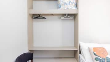 Een slaapkamer met een bed, een stoel, een kledingkast met planken en een hangroede.
