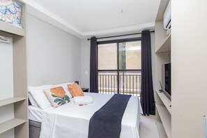 A modern hotel room with a bed, a TV, a balcony with curtains, and a view of the outside. - Studio com Sacada All You Need ALL0305 (Curitiba)