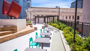 An outdoor seating area with tables and chairs, a red sculpture, and a building with classical architecture in the background. - Studio com Sacada All You Need ALL0305 (Curitiba)