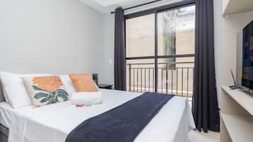 Una habitación de hotel con cama, televisor, ventana con cortinas y balcón.