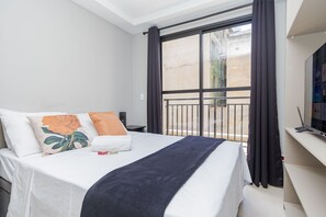 A hotel room with a bed, a TV, a window with curtains, and a balcony. - Studio com Sacada All You Need ALL0305 (Curitiba)