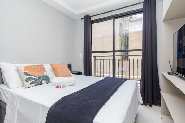 A hotel room with a bed, a TV, a window with curtains, and a balcony.