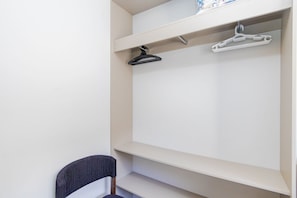 A corner of a room with a white closet, two hangers, and a chair. - Studio com Sacada All You Need ALL0305 (Curitiba)