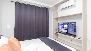 Quarto de hotel com cama, televisão sobre um suporte, ar condicionado na parede e cortina.