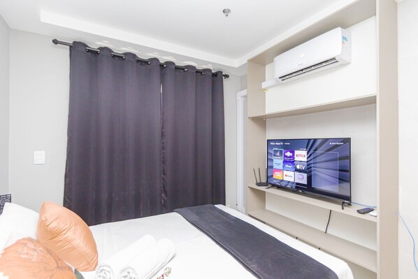 A hotel room with a bed, a TV on a stand, a wall-mounted air conditioner, and a curtain. - Studio com Sacada All You Need ALL0305 (Curitiba)