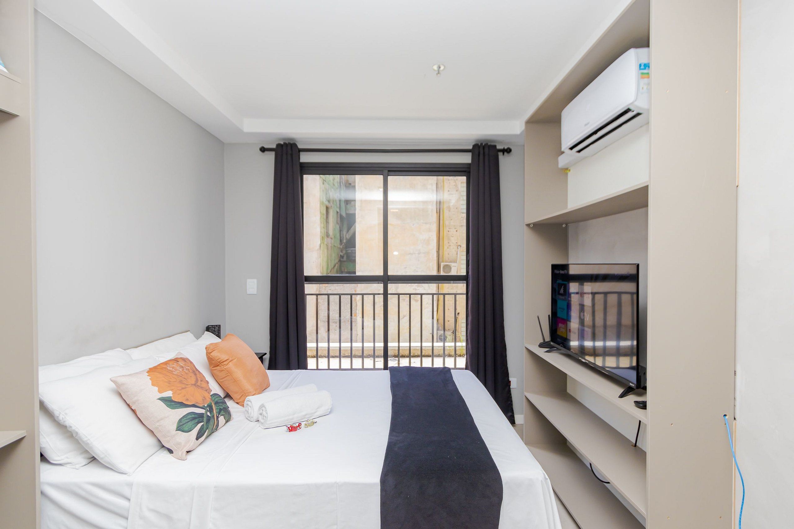 Una habitación de hotel con cama, televisión y balcón con barandilla.