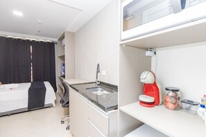 Quarto de hotel com uma cama, pequeno espaço de cozinha, cafeteira e um pote de lanches.