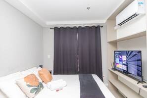 A hotel room with a bed, a flat-screen TV, a wall-mounted air conditioner, and a curtain. - Studio com Sacada All You Need ALL0305 (Curitiba)