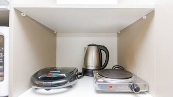 A kitchen with a coffee maker, a kettle, and a rice cooker on a white countertop.