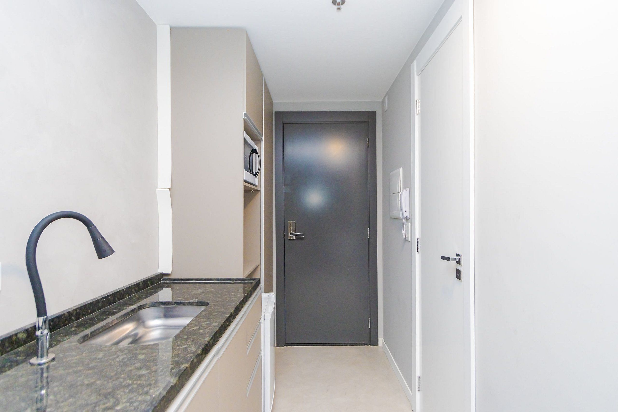 A narrow hallway with a kitchen area on the left, including a sink and countertop. A door is visible at the end of the hallway.