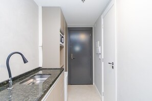 A narrow hallway with a kitchen area on the left, including a sink and countertop. A door is visible at the end of the hallway. - Studio com Sacada All You Need ALL0305 (Curitiba)