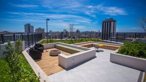 Une terrasse sur le toit, aménagée avec des espaces salon, un foyer et offrant une vue sur le panorama urbain.
