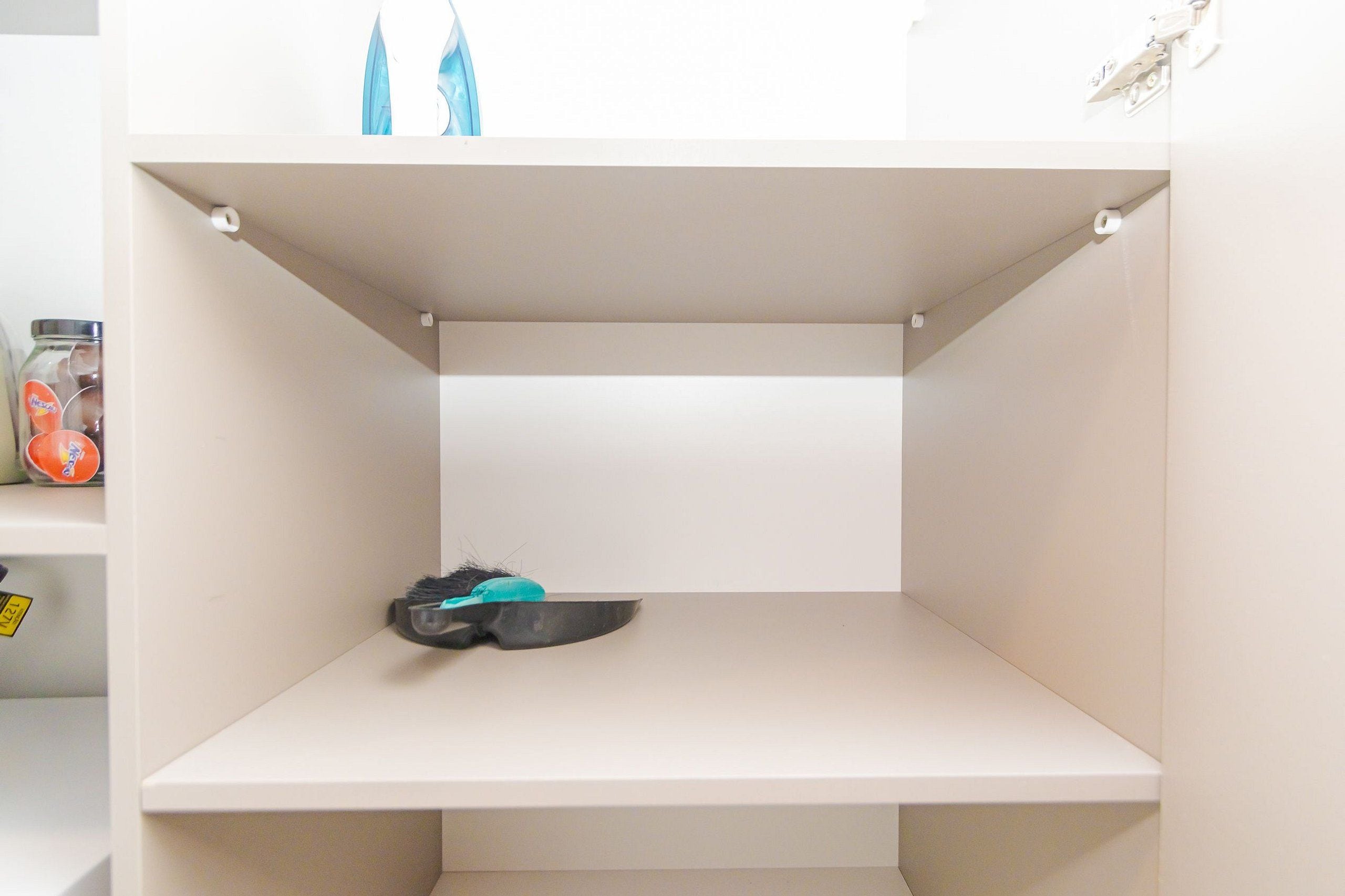 Una estantería blanca con un par de tijeras y un pequeño recipiente.