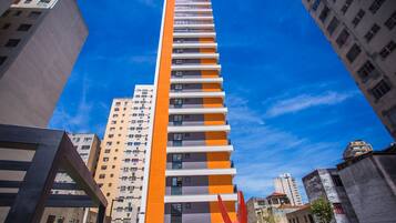 Un edificio alto y moderno con una fachada distintiva de color naranja y blanco, rodeado de otros edificios.