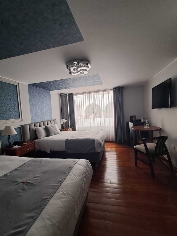 A hotel room with two beds, a desk, a chair, a TV, and a window with curtains. - Hotel Fundador By Robles (Arequipa)
