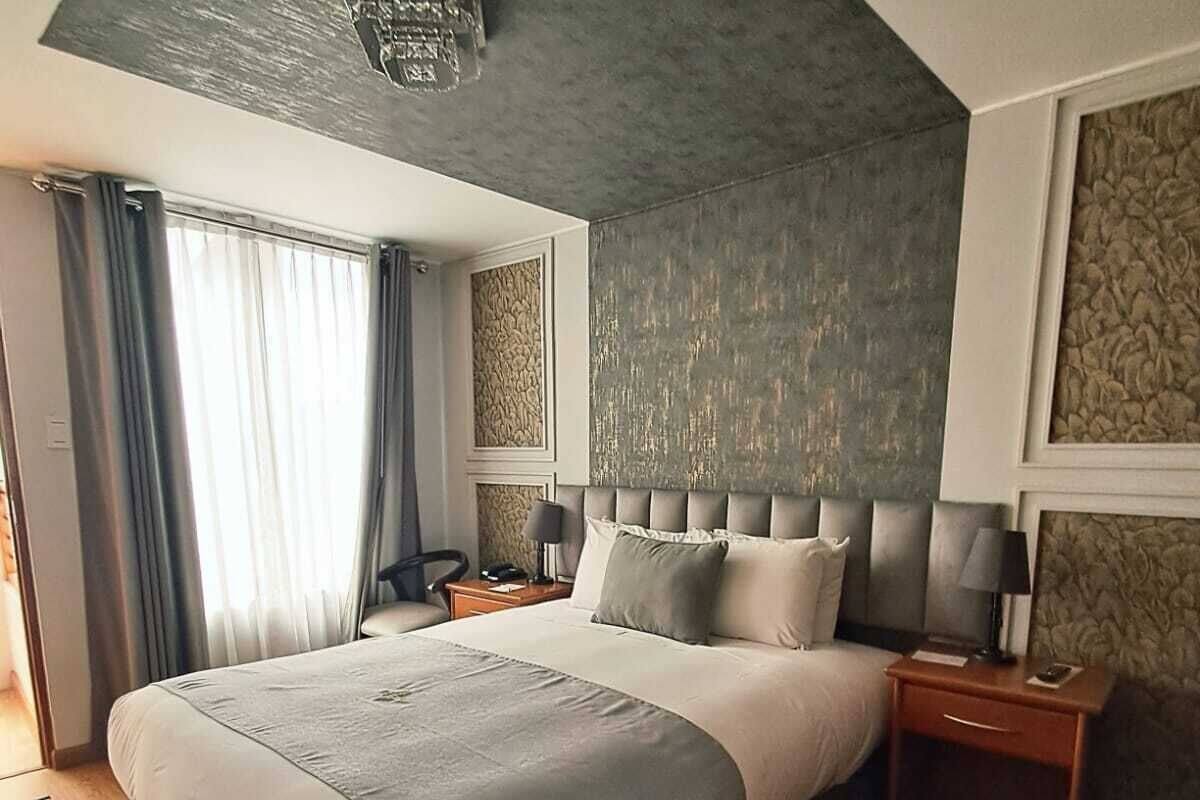 Habitación de hotel moderna con una cama grande, suelo de madera, luz de techo, mesita de noche y una ventana con cortinas.