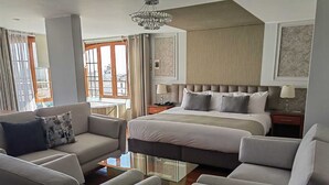 A modern hotel room with a large bed, two bedside tables, a sofa, and a glass coffee table. - Hotel Fundador By Robles (Arequipa)