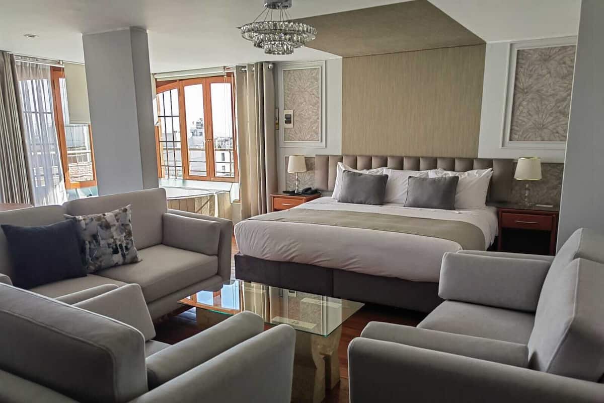 Una habitación de hotel moderna con una cama grande, dos mesitas de noche, un sofá y una mesa de centro de vidrio.
