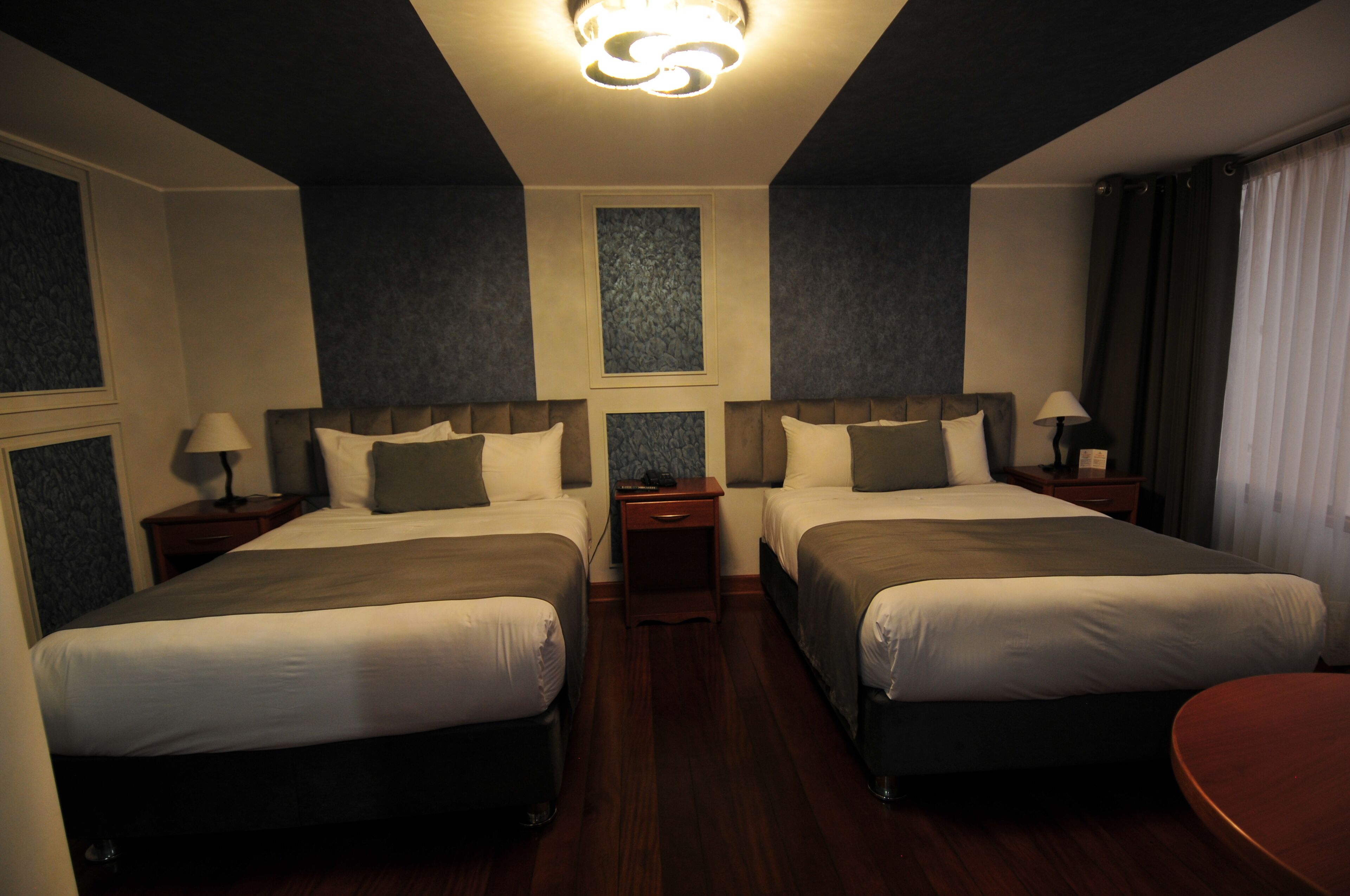 A hotel room with two beds, a small table, and a nightstand with lamps.