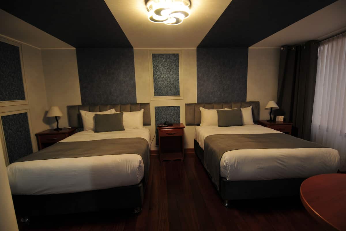 Una habitación de hotel con dos camas, una mesita pequeña y una mesita de noche con lámparas.