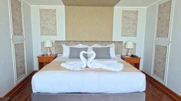 A large bed with a heart-shaped towel arrangement, wooden flooring, and a neutral color scheme.