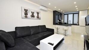 A modern living room with a black sofa, a white coffee table, and a kitchen area with a bar counter and two white bar stools. - Apartment by Luxe Group SA222 (Yerevan)