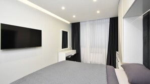 A modern hotel room with a large bed, a flat-screen TV mounted on the wall, a bedside table, and a window with sheer curtains. - Apartment by Luxe Group SA222 (Yerevan)