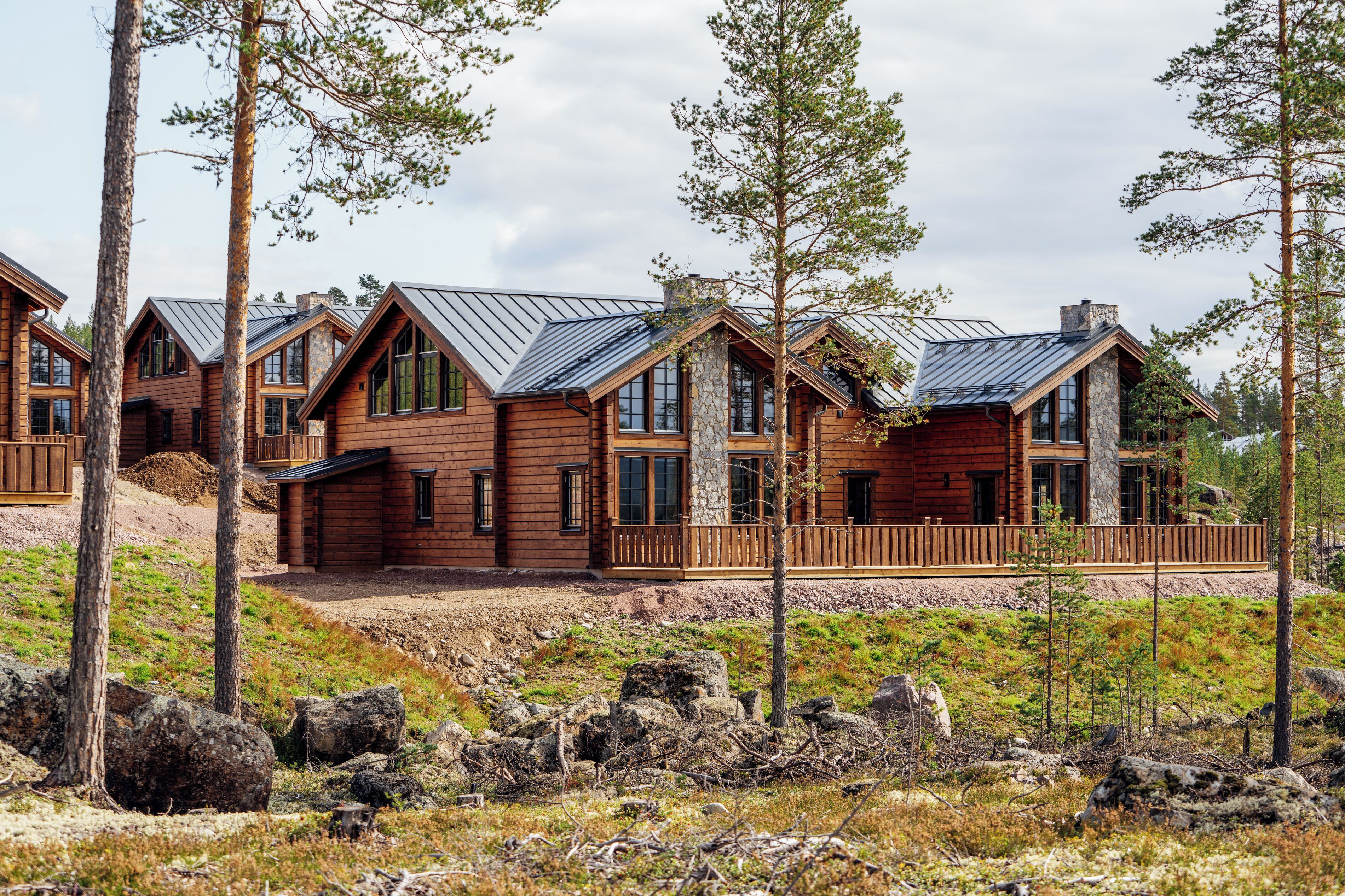 Une cabane en rondins avec un toit en métal, de nombreuses fenêtres et une terrasse en bois.