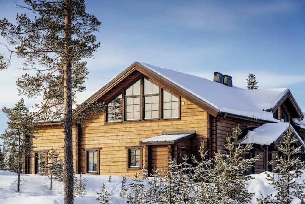 A wooden cabin with large windows and a sloped roof, surrounded by snow-covered trees.