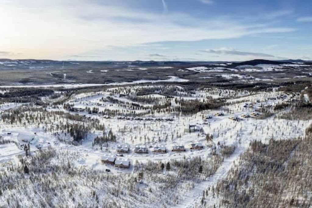Un paysage enneigé avec un ensemble de bâtiments, probablement un complexe hôtelier ou un chalet, entouré de forêts denses.