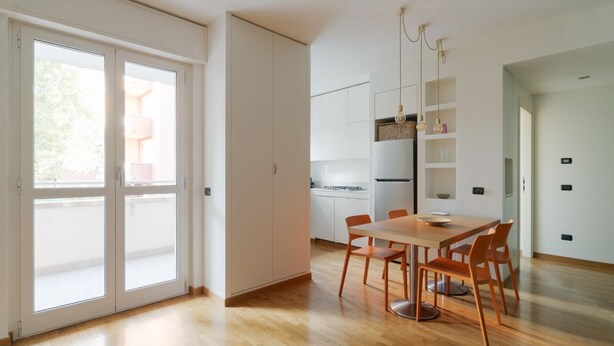 A modern kitchen with white cabinets, a wooden dining table, and orange chairs. - GuestHost - Bright Apartment M1 Precotto Milano (Milan)