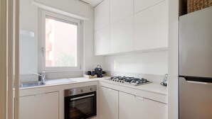 A compact kitchen with white cabinetry, a built-in oven, a gas stove, and a window providing natural light. - GuestHost - Bright Apartment M1 Precotto Milano (Milan)