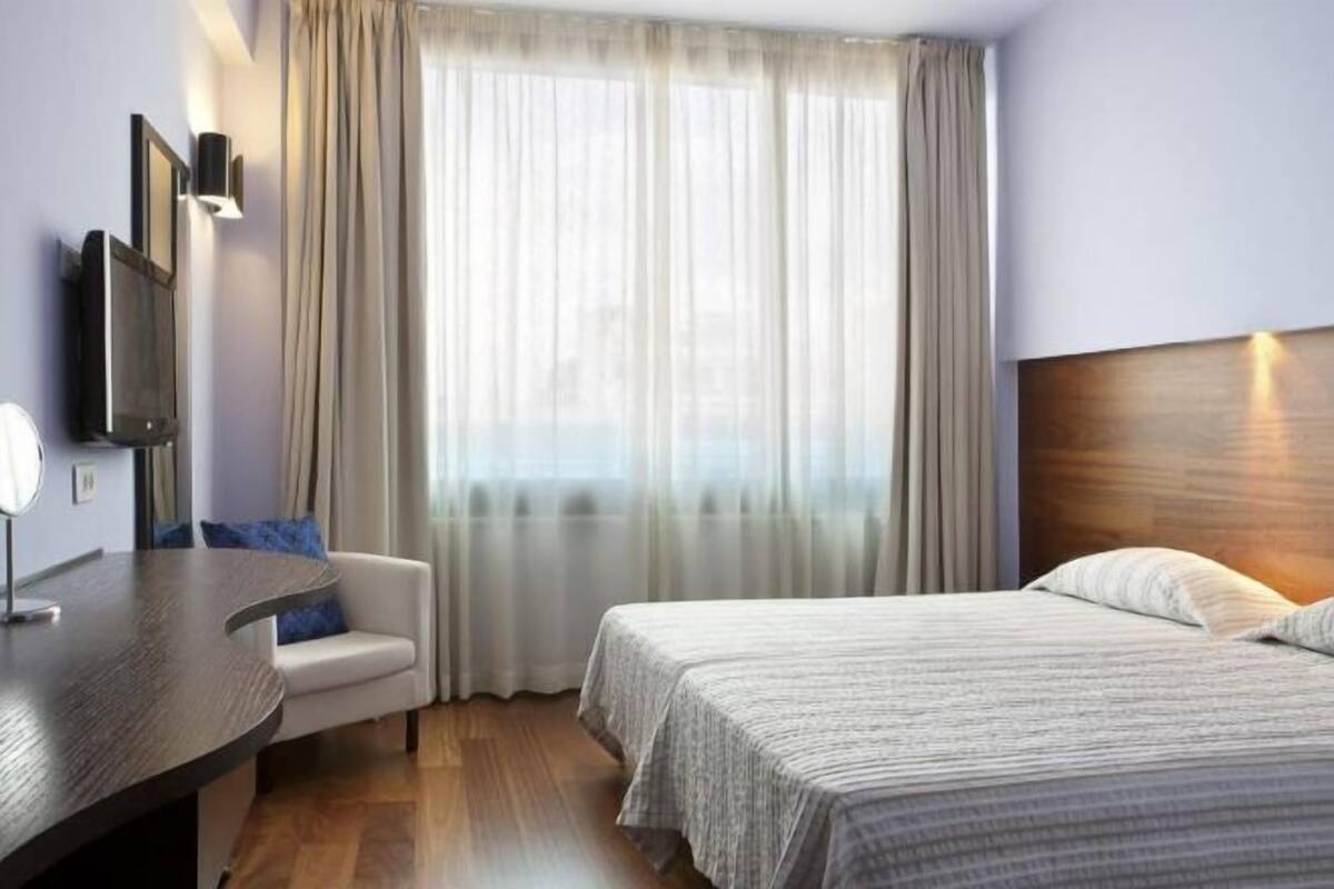 A hotel room with a bed, a desk, a chair, and a TV.
