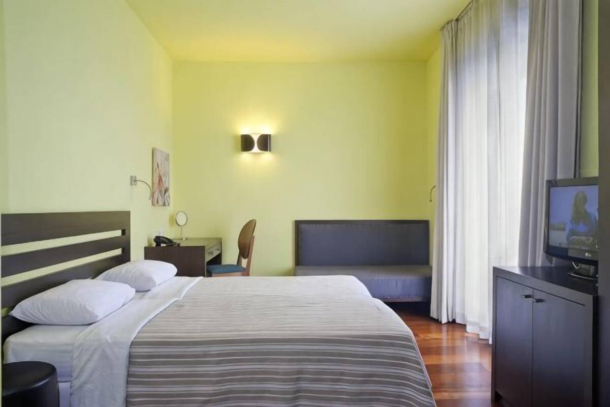 A hotel room with a bed, a desk, a television, and a window with curtains.
