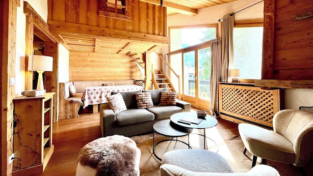 Interior acolhedor de uma cabana de madeira, com um sofá, poltronas, uma mesa e uma lareira.