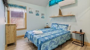 A bedroom with a bed, a window with blinds, a shelf with decorative items, and a small table with a lamp. - 3 Usen Lane near all the fun (Old Orchard Beach)