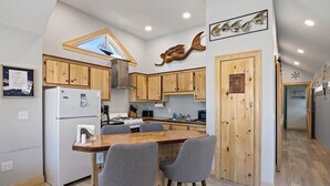 A modern kitchen with wooden cabinets, a central island with bar stools, a built-in stove, and a window above the sink. - 3 Usen Lane near all the fun (Old Orchard Beach)