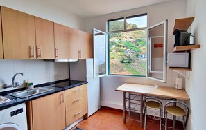 A compact kitchen with wooden cabinets, a built-in oven, a sink, and a window offering a view of a hillside. - Villa Rodrigues 1 by Rentallido (Campanario)