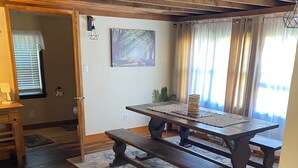 Un comedor con una mesa de madera y bancos, una alfombra y un cuadro en la pared.