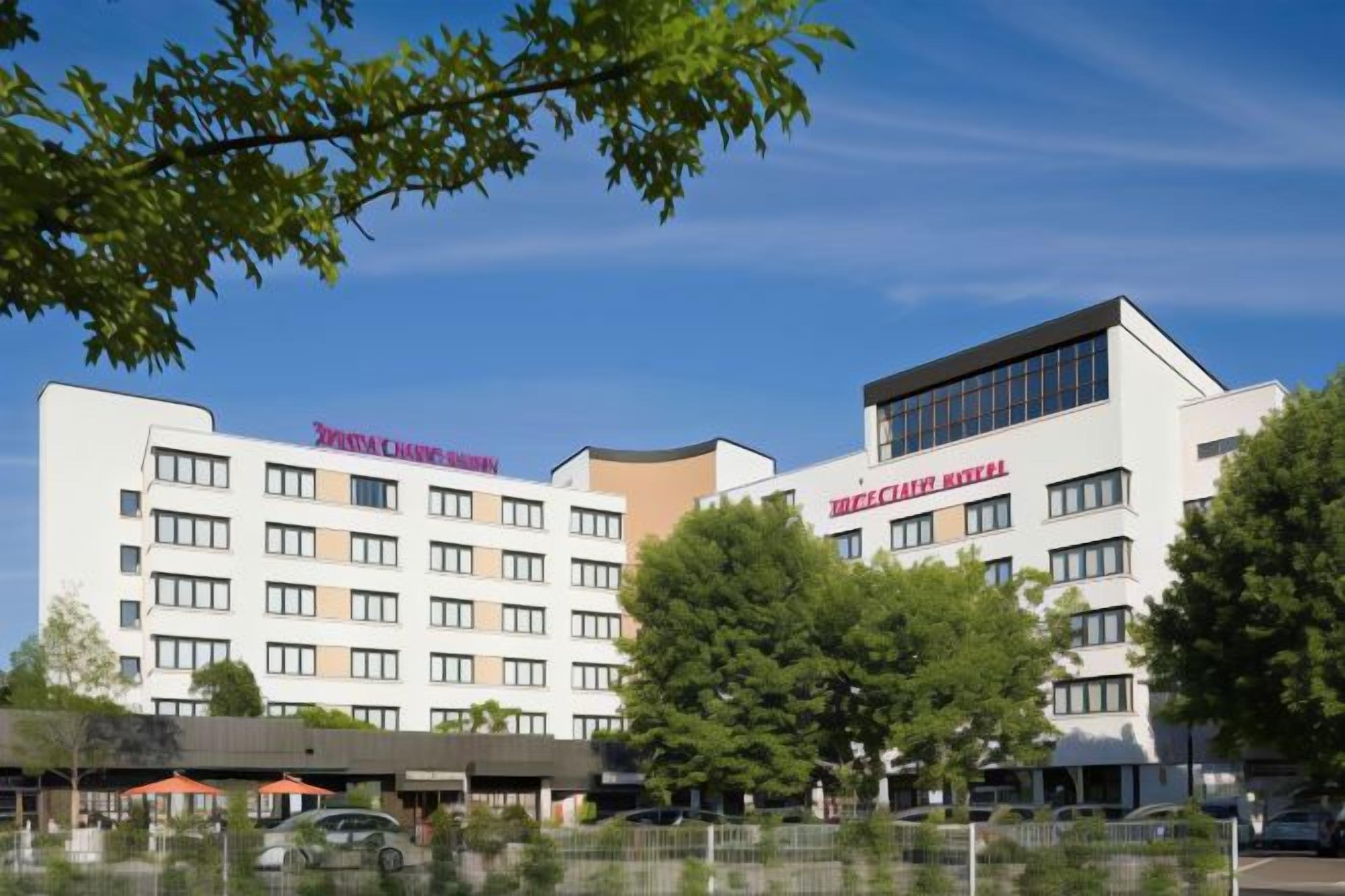 A hotel with multiple floors, a flat roof, and a parking area in front.